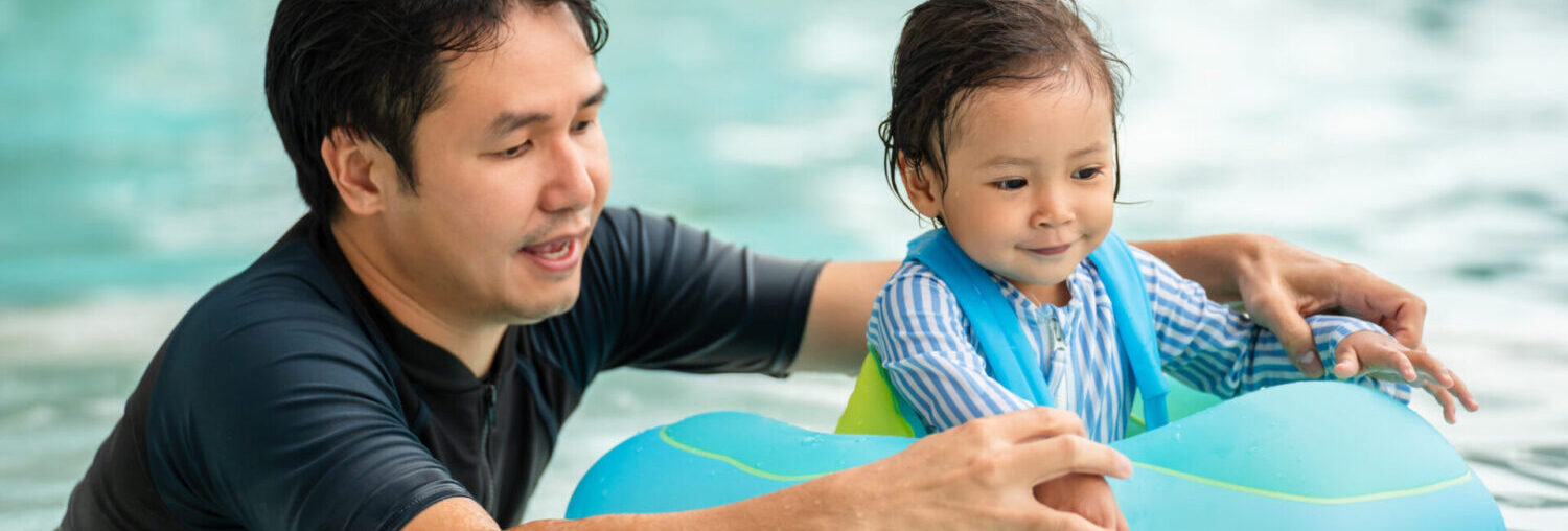 happy father with toddler baby girl playing in an inflatable ring in swimming pool